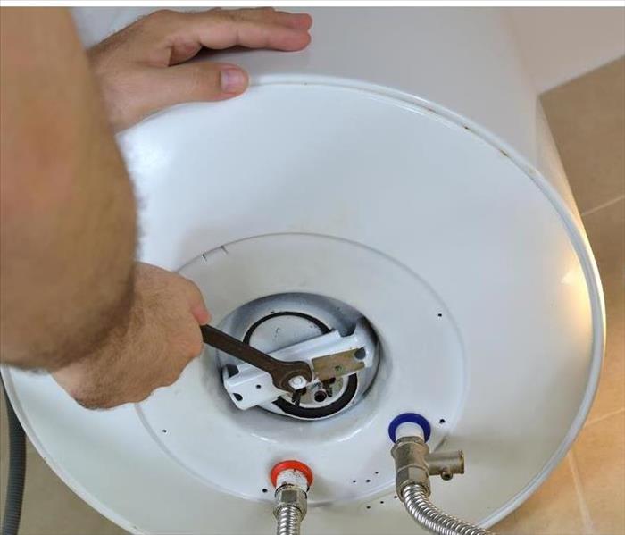 Man's hands unscrewing a screw-nut on a water heater with a wrench on a boiler