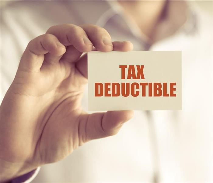 Closeup on businessman holding a card with text TAX DEDUCTIBLE,